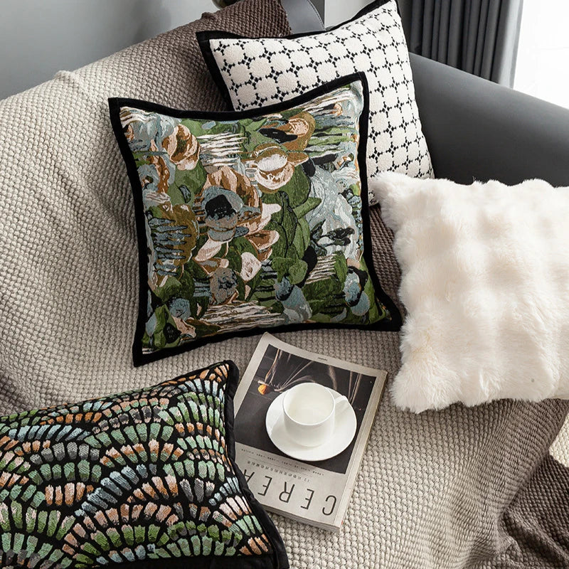 Coussin décoratif fleuri sur un canapé gris avec un livre et une tasse blanche sur une table basse, créant une atmosphère cosy et élégante.