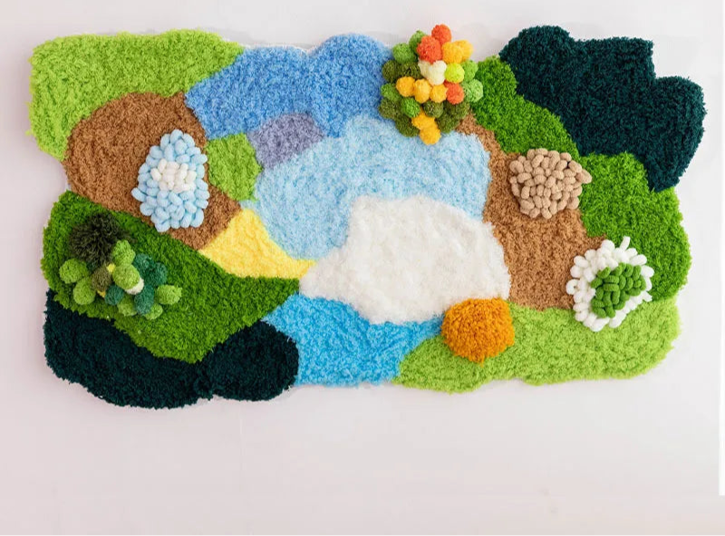 Un paysage coloré et texturé composé de différents matériaux comme du feutre, des pompons et du gazon artificiel, créant une scène naturelle pleine de vie et de couleurs.