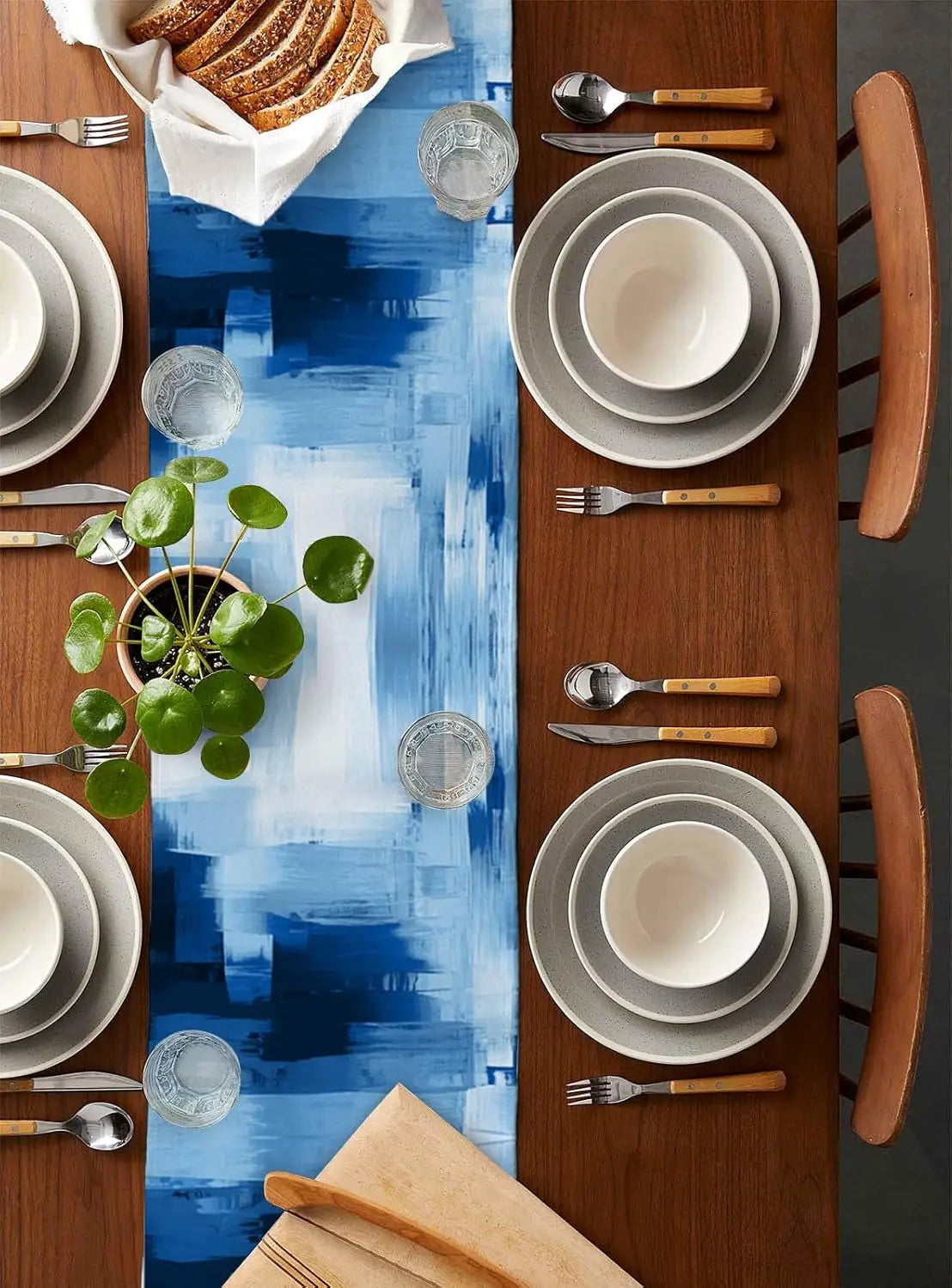 Une belle table de repas avec des assiettes, couverts et plantes décoratifs sur un fond de couleur bleue et bois.