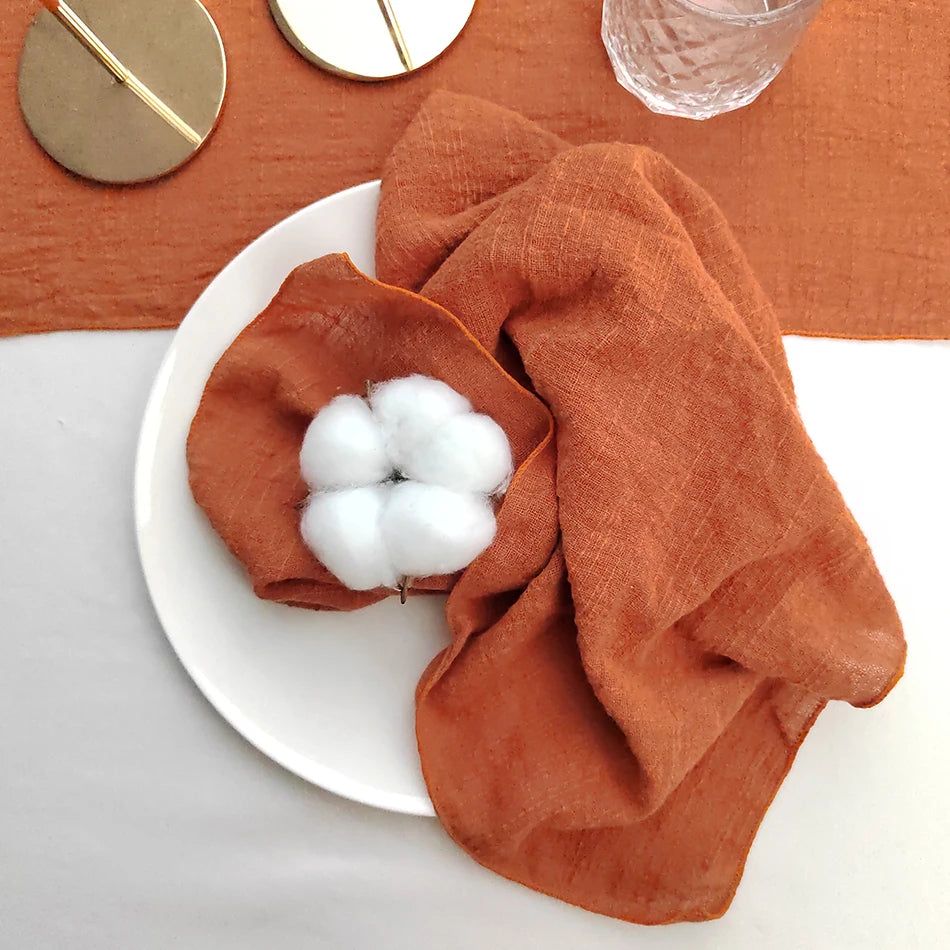 Une serviette en lin orange enveloppant un bouquet de coton blanc, posée sur une table en bois avec des accessoires de salle de bain.