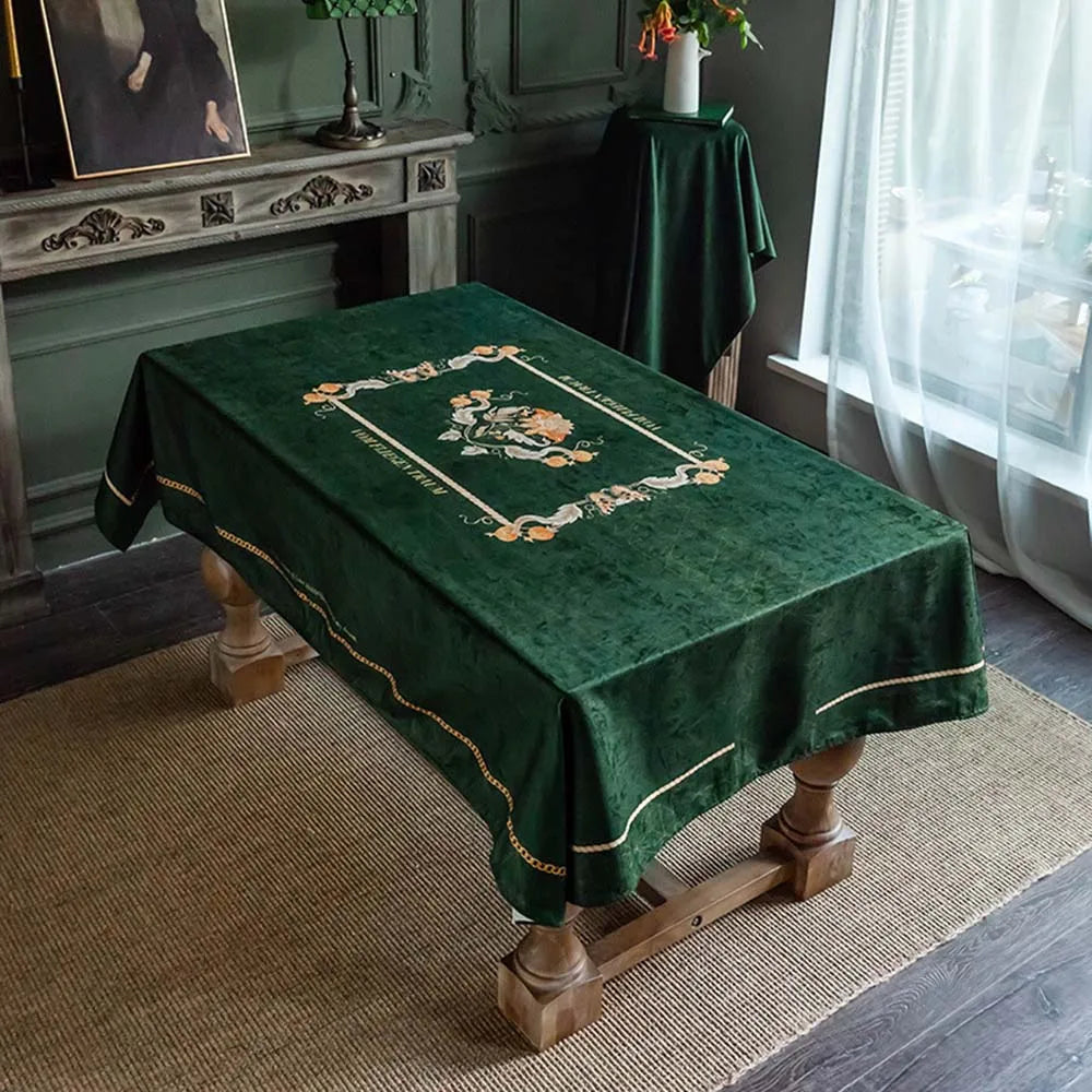 Élégante table recouverte d'une nappe verte ornée de motifs floraux délicats et bordée d'une belle dentelle dorée, créant une atmosphère chic et raffinée dans cette pièce à l'ambiance vintage.