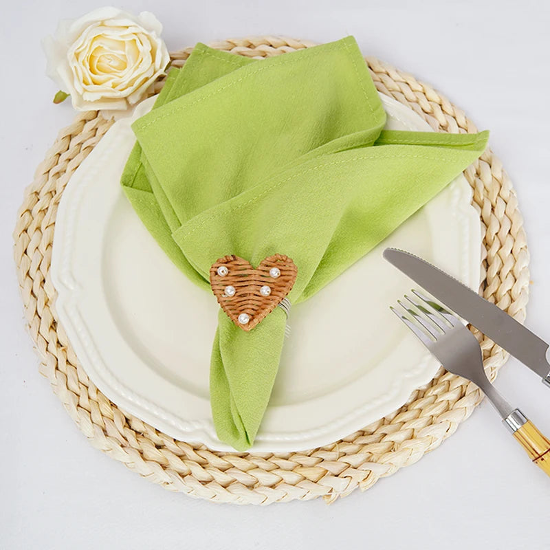 Assiette blanche avec une serviette verte et un coeur décoratif en bois sur une natte en osier, accompagnée d'une rose blanche.