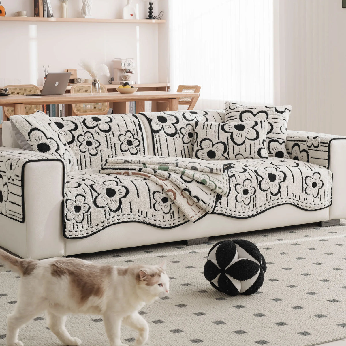 Un canapé avec un motif floral blanc et noir, posé sur un tapis à motifs géométriques, avec un chat blanc dans le salon lumineux.