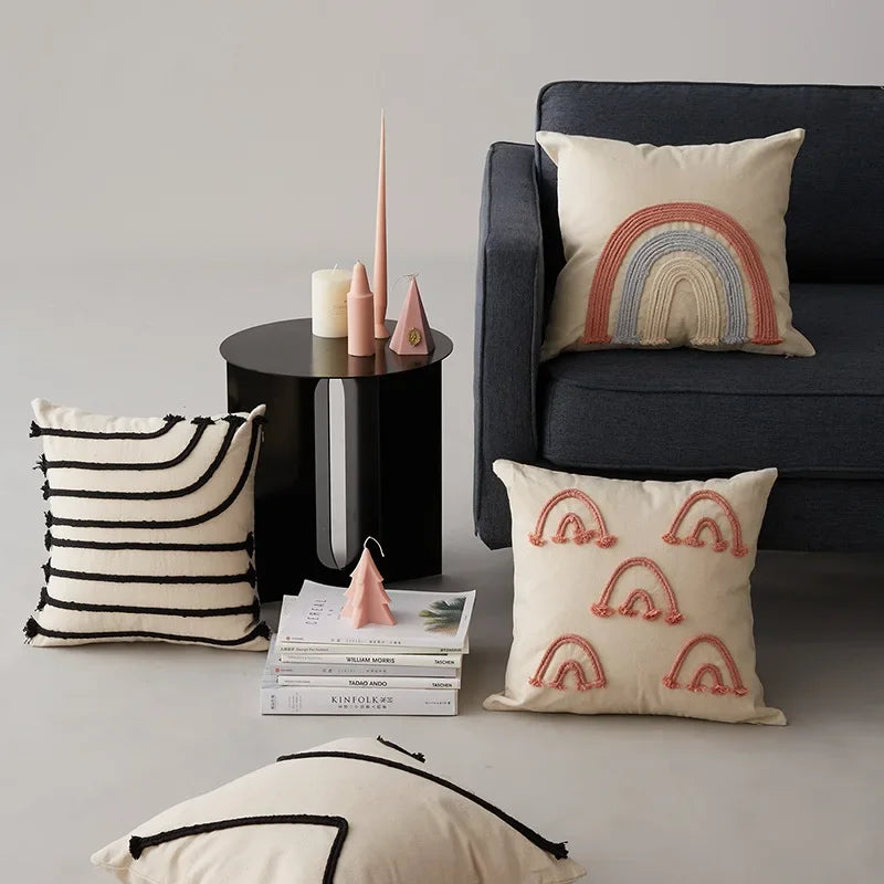 Décor tendance avec des coussins aux motifs arc-en-ciel, des livres et des accessoires de style moderne sur un canapé sombre.