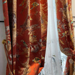 Rideau à motifs tropicaux orangé avec détails animaliers et feuillages dorés, retenu par une embrasse dorée et accompagné d’un voilage blanc délicat.