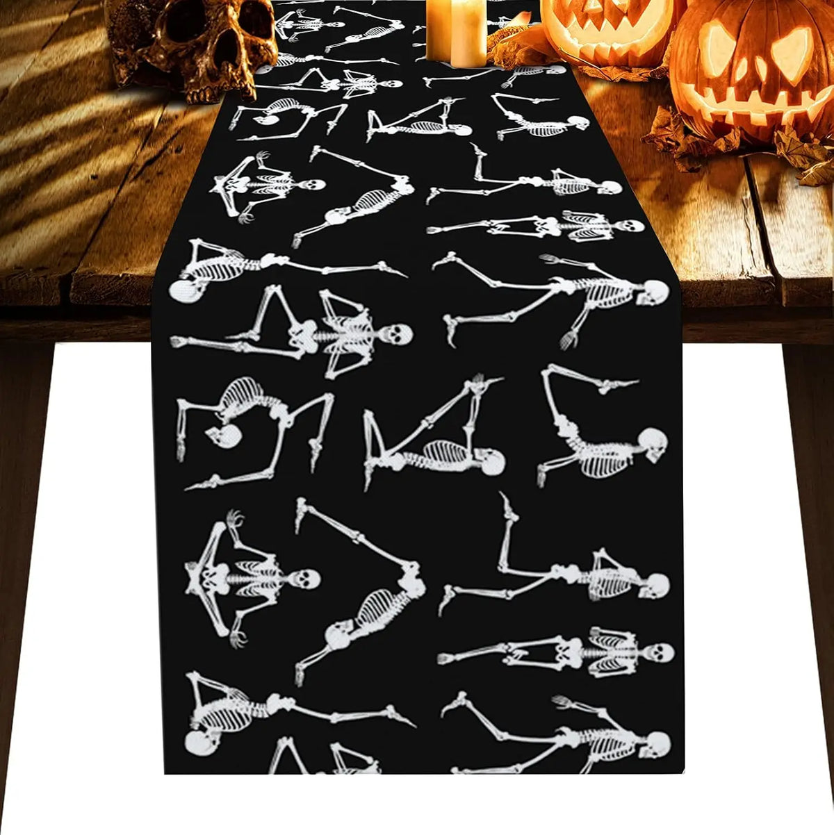 Une nappe de table décorée d'un motif squelettique en noir et blanc, entourée de citrouilles sculptées et de bougies allumées, créant une ambiance mystérieuse et effrayante parfaite pour une soirée d'Halloween.