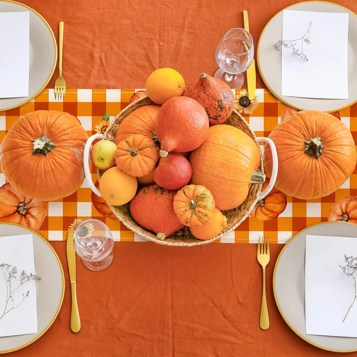 Une belle composition automnale avec des citrouilles, des pommes et des fleurs, disposés sur une nappe vichy orange, créant une ambiance chaleureuse et festive.