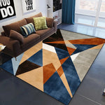 Un tapis avec un motif géométrique moderne et coloré, composé de triangles bleus, oranges et gris, qui crée une ambiance élégante et épurée dans cette pièce d'intérieur.