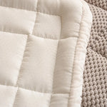 Cette image montre un gros plan sur un tissu douillet et matelassé, avec une texture de points cousus formant un motif de carrés réguliers. Le tout est posé sur une surface tricotée en maille, ajoutant une touche de chaleur et de confort à l'ensemble.