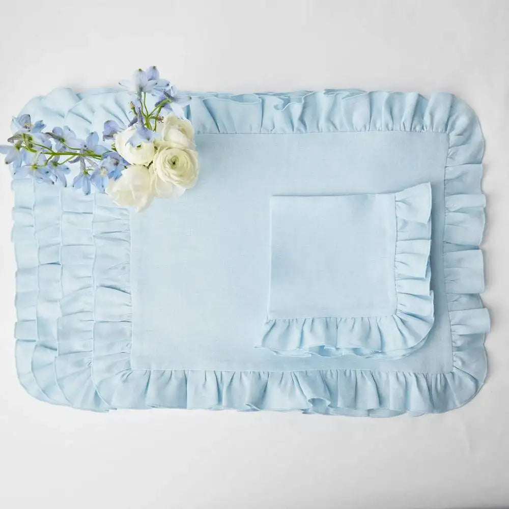 Cet ensemble de literie délicat comprend un drap plat et une taie d'oreiller ornés de volants, avec un bouquet de fleurs pastel posé délicatement dessus, créant une ambiance élégante et apaisante.