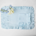 Cet ensemble de literie délicat comprend un drap plat et une taie d'oreiller ornés de volants, avec un bouquet de fleurs pastel posé délicatement dessus, créant une ambiance élégante et apaisante.