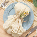 Une assiette bleue avec un linge décoratif blanc attaché d'une ficelle et orné de petites fleurs, prêt pour une belle présentation de table.