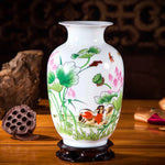 Vase en céramique blanc orné de motifs peints de lotus, de feuilles vertes et d'animaux aquatiques, sur un socle en bois sombre, créant une image exotique et paisible.