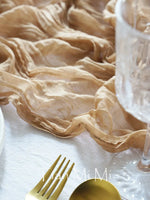 Le détail texturé et élégant de ce textile crème fait ressortir les couverts dorés sur la nappe blanche, créant une atmosphère raffinée et harmonieuse.