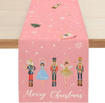 Une nappe de table de Noël rose décorée de figurines féériques comme le casse-noisette, la fée, la danseuse et le soldat, créant une atmosphère enchantée pour les fêtes de fin d'année.