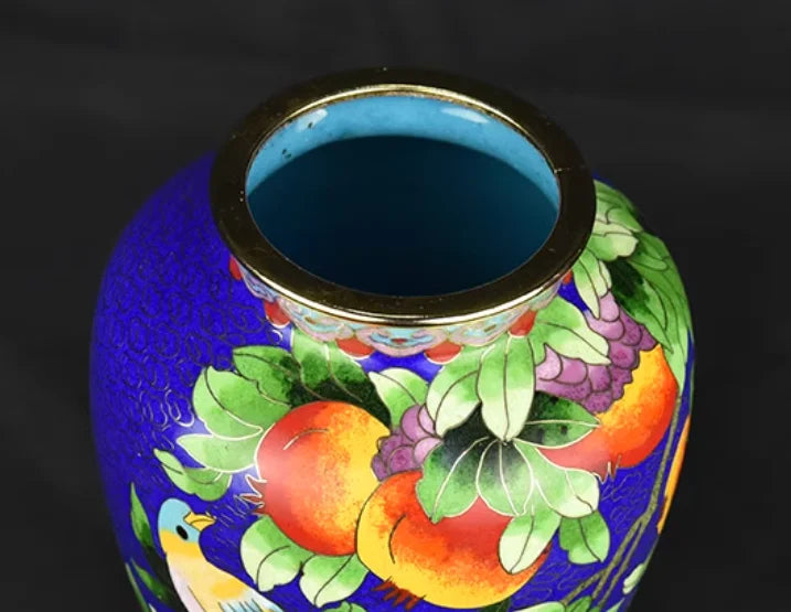 Vase décoratif en céramique peint de motifs colorés de fruits, fleurs et feuilles sur un fond bleu vif.