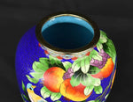 Vase décoratif en céramique peint de motifs colorés de fruits, fleurs et feuilles sur un fond bleu vif.