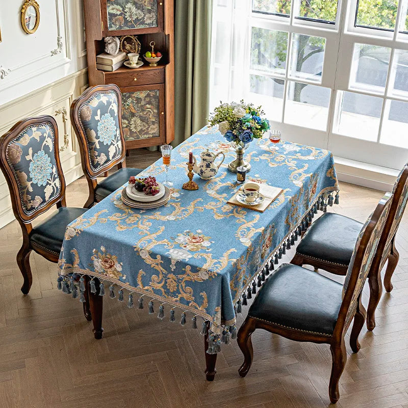 Une table élégante et ornée dans un intérieur vintage, avec une nappe bleue et dorée, des chaises sculptées et des décorations raffinées.