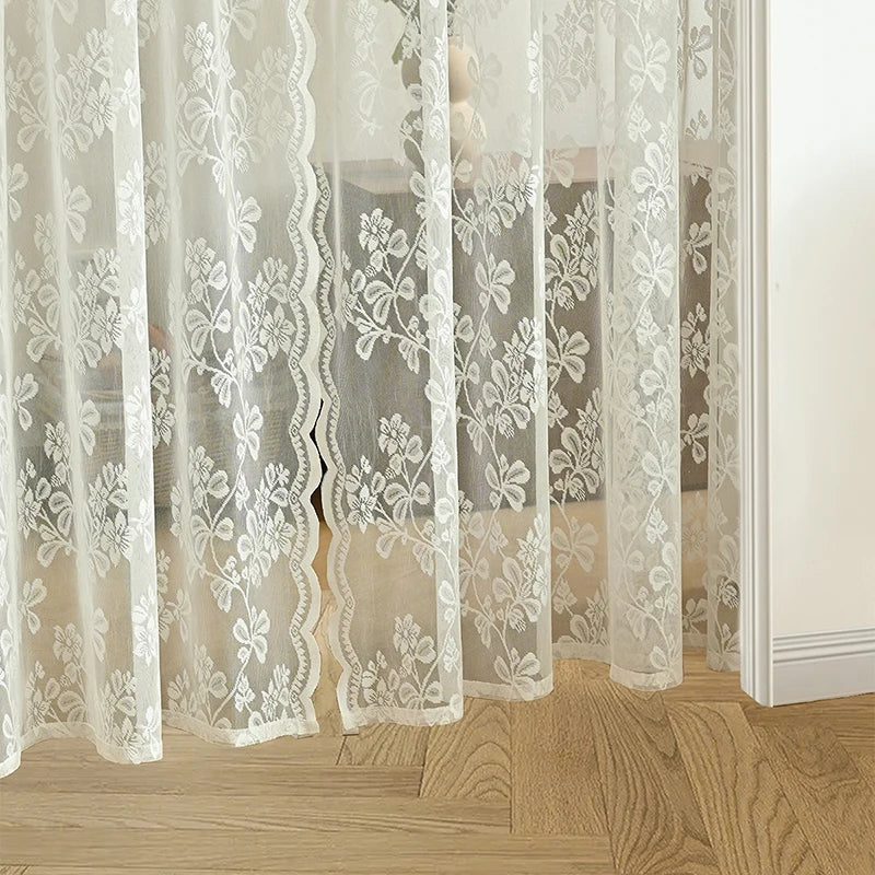 Voilage en dentelle blanche à motifs floraux posé devant un sol en parquet clair