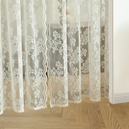 Voilage en dentelle blanche à motifs floraux posé devant un sol en parquet clair
