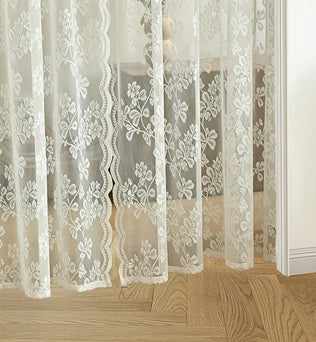 Voilage en dentelle blanche à motifs floraux posé devant un sol en parquet clair