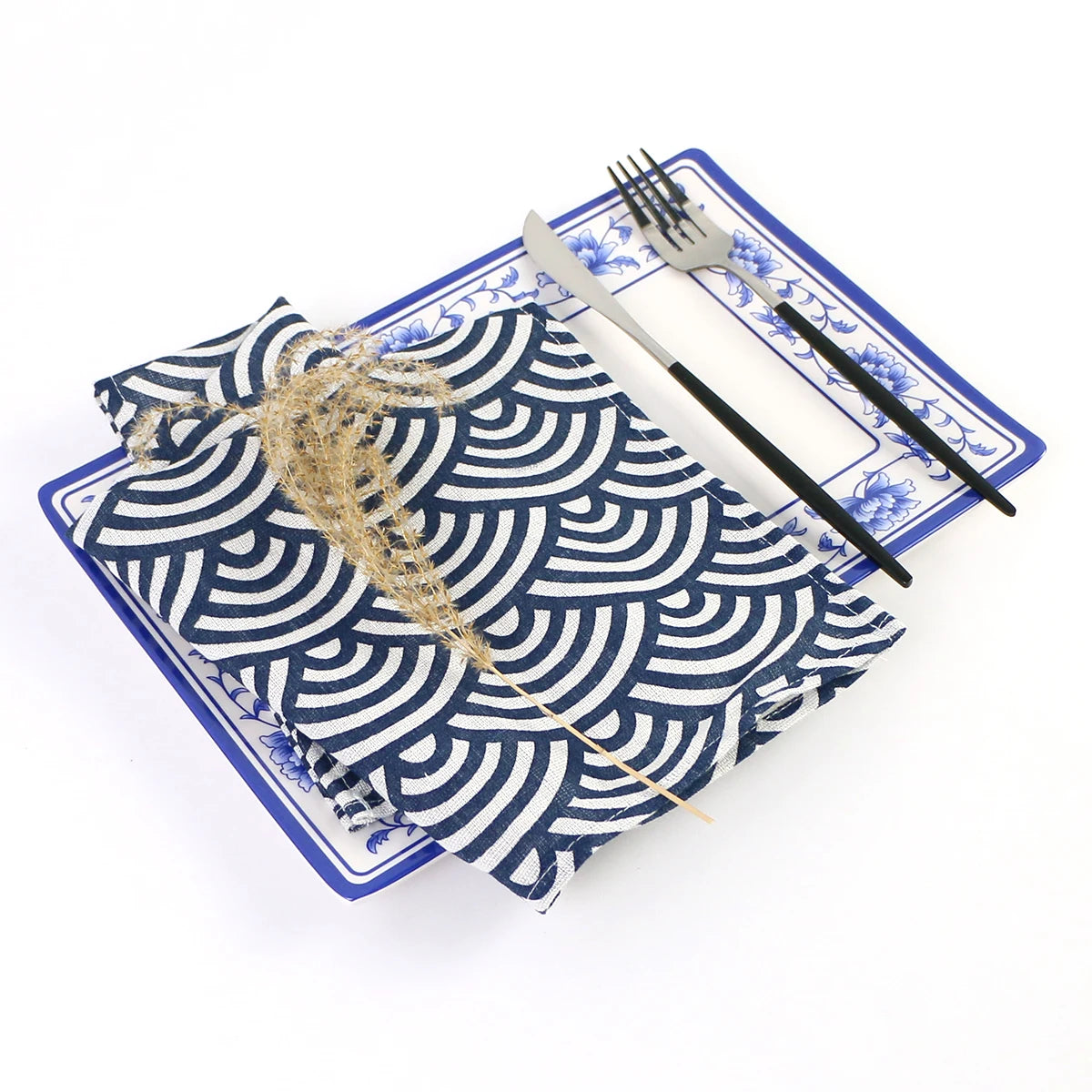 Un service de table avec une nappe à motifs géométriques bleus et blancs, accompagné de couverts en métal et d'un élément décoratif en raphia.