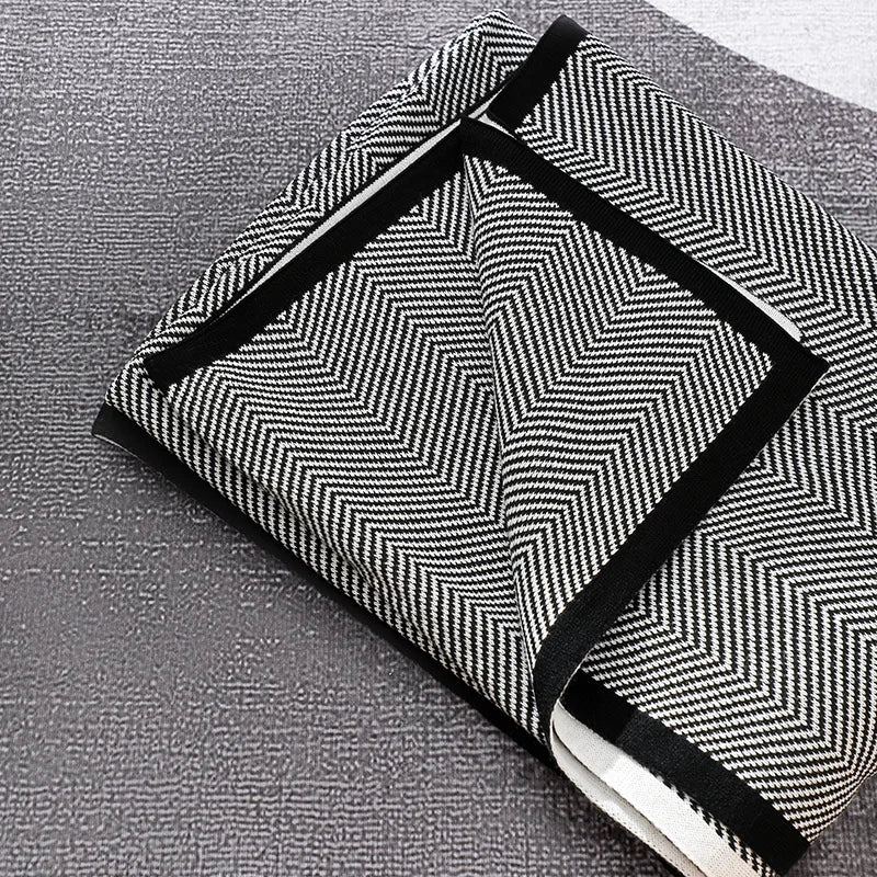 Un sac élégant noir et blanc orné de motifs géométriques, avec des poignées noires, posé sur une surface grise.