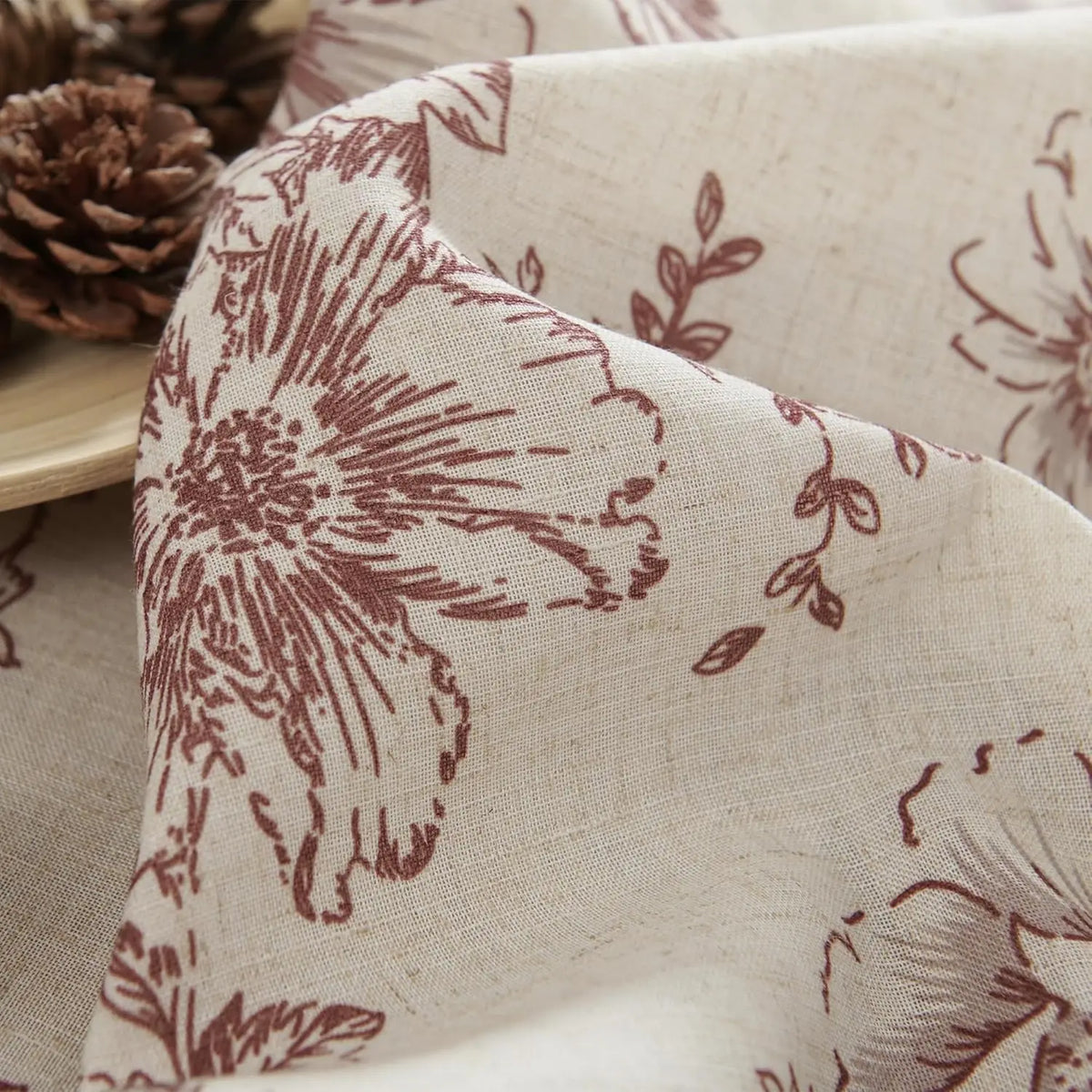 Gros plan du tissu à fleurs bordeaux sur fond beige, mettant en valeur la texture naturelle du rideau.