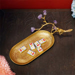 Un élégant plateau doré décoré d'un oiseau en métal et de cristaux violets, sur lequel reposent des chocolats emballés dans des films dorés.