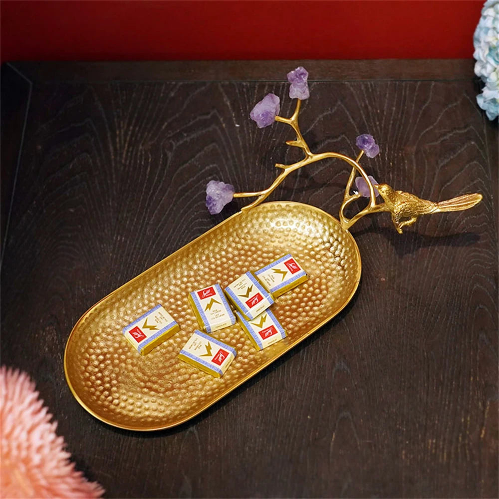 Un élégant plateau doré décoré d'un oiseau en métal et de cristaux violets, sur lequel reposent des chocolats emballés dans des films dorés.