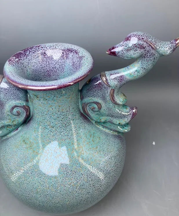 Un vase en céramique de couleur vert pâle, avec des taches violettes, doté de motifs en spirale sur les côtés et d'une salamandre en relief.