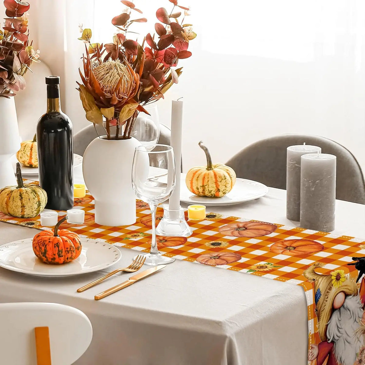 La photographie montre une table élégamment décorée pour une occasion spéciale, avec un bouquet de fleurs automnales, une bouteille de vin rouge, des verres à vin, des bougies et des citrouilles décorant la scène.