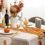 La photographie montre une table élégamment décorée pour une occasion spéciale, avec un bouquet de fleurs automnales, une bouteille de vin rouge, des verres à vin, des bougies et des citrouilles décorant la scène.