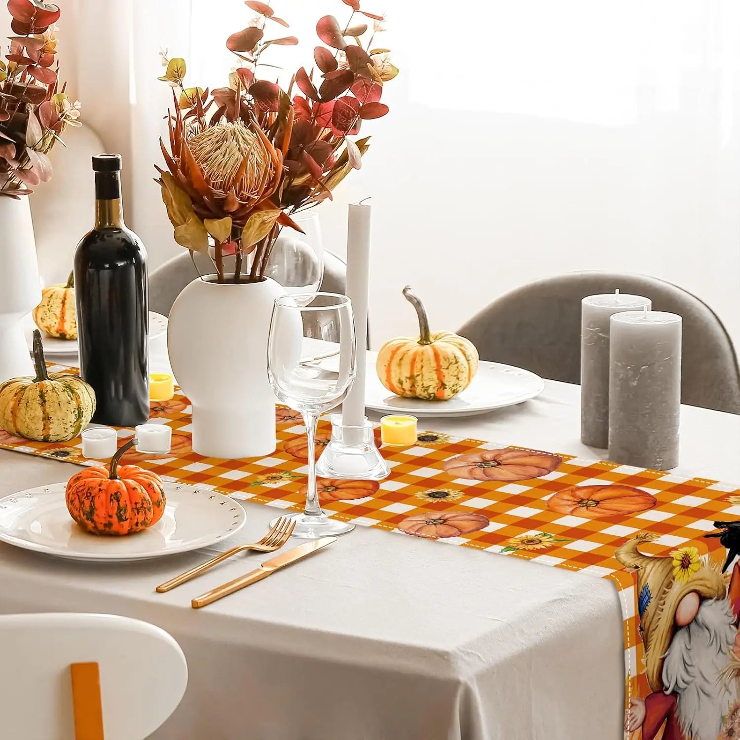 La photographie montre une table élégamment décorée pour une occasion spéciale, avec un bouquet de fleurs automnales, une bouteille de vin rouge, des verres à vin, des bougies et des citrouilles décorant la scène.