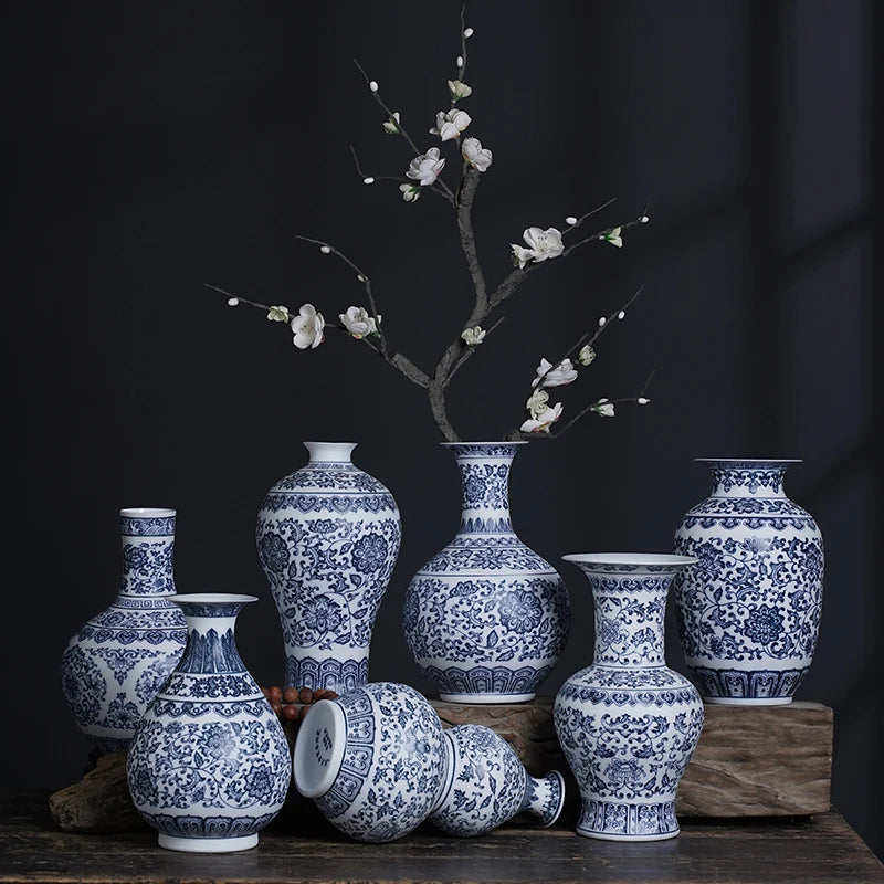 Une collection de vases en porcelaine anciens à motifs bleus et blancs, exposés avec une branche fleurie sur un fond sombre.