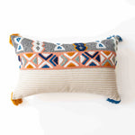 Coussin décoratif aux motifs géométriques multicolores sur fond blanc avec des franges.