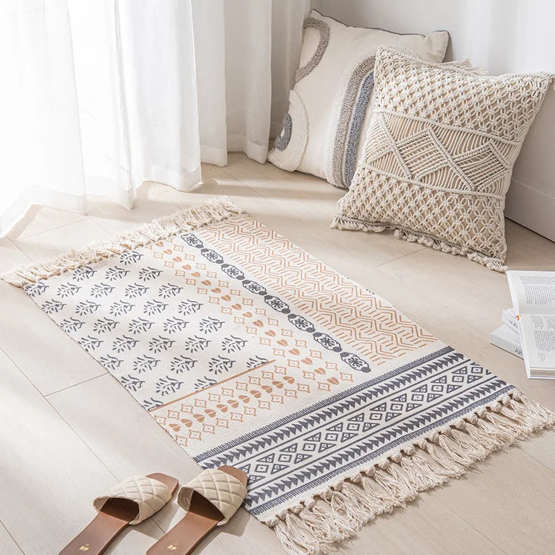 Un tapis orné de motifs ethniques avec des franges dans un intérieur lumineux, accompagné de coussins décoratifs et de sandales beiges, créant une ambiance chaleureuse et apaisante.