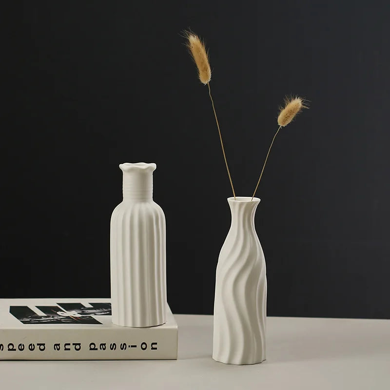 Deux vases blancs sculptés posés sur une surface avec des épis de blé dorés, créant une composition élégante et minimaliste sur un fond noir.