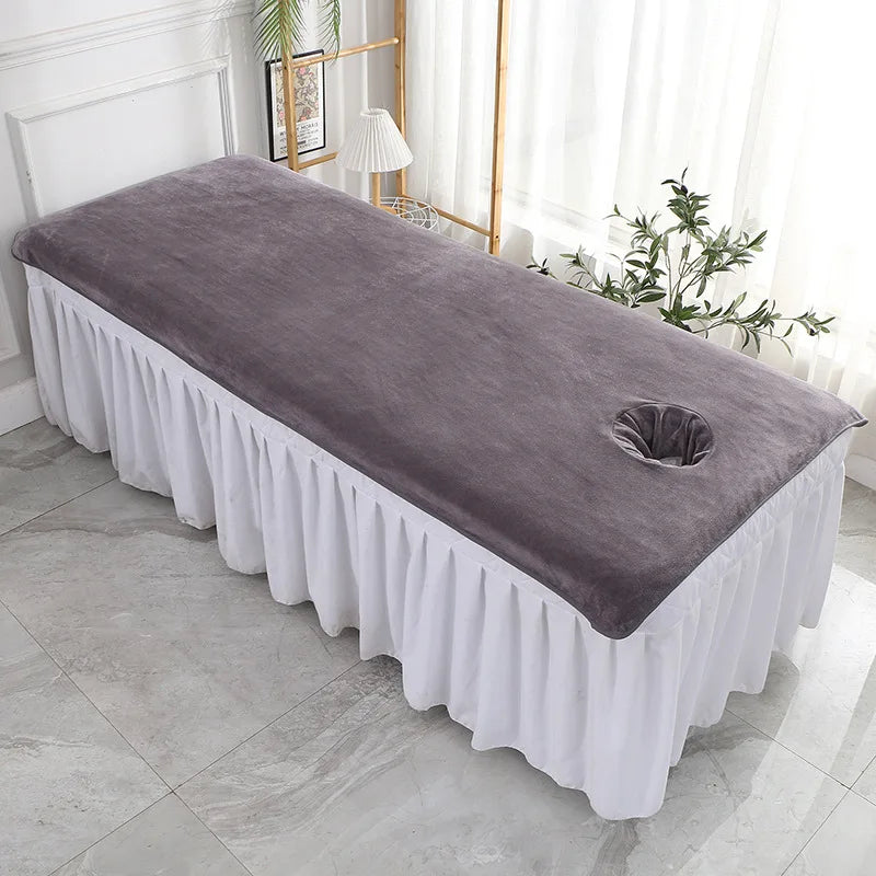 Un lit de massage douillet avec une housse en velours gris et une décoration végétale discrète, créant une ambiance sereine et relaxante.