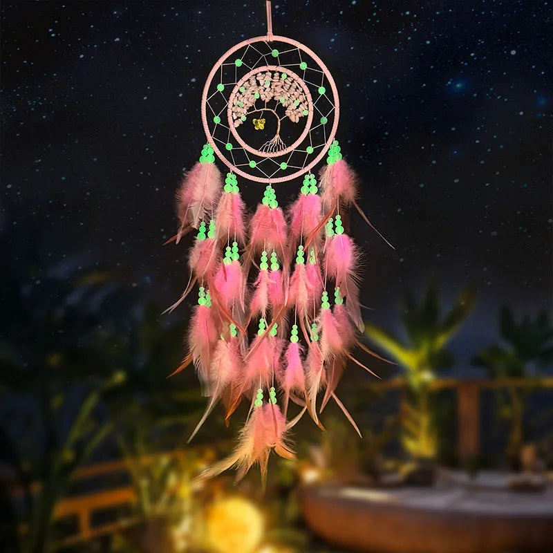 Un capteur de rêves rose et vert, avec un arbre de vie au centre, décoré de plumes et de perles, suspendu dans un ciel étoilé.