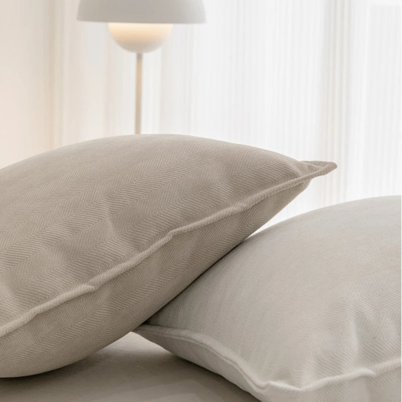Deux oreillers gris clair sur un lit, éclairés par une lampe de plancher en arrière-plan.