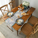 Une table en bois avec une belle nappe colorée, des assiettes avec des couverts et un panier de délicieux pains sur un tapis moelleux, créant une atmosphère accueillante et chaleureuse pour un repas.