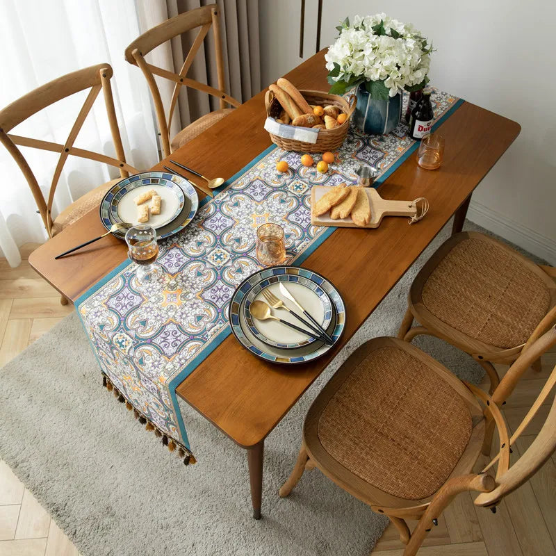 Une table en bois avec une belle nappe colorée, des assiettes avec des couverts et un panier de délicieux pains sur un tapis moelleux, créant une atmosphère accueillante et chaleureuse pour un repas.