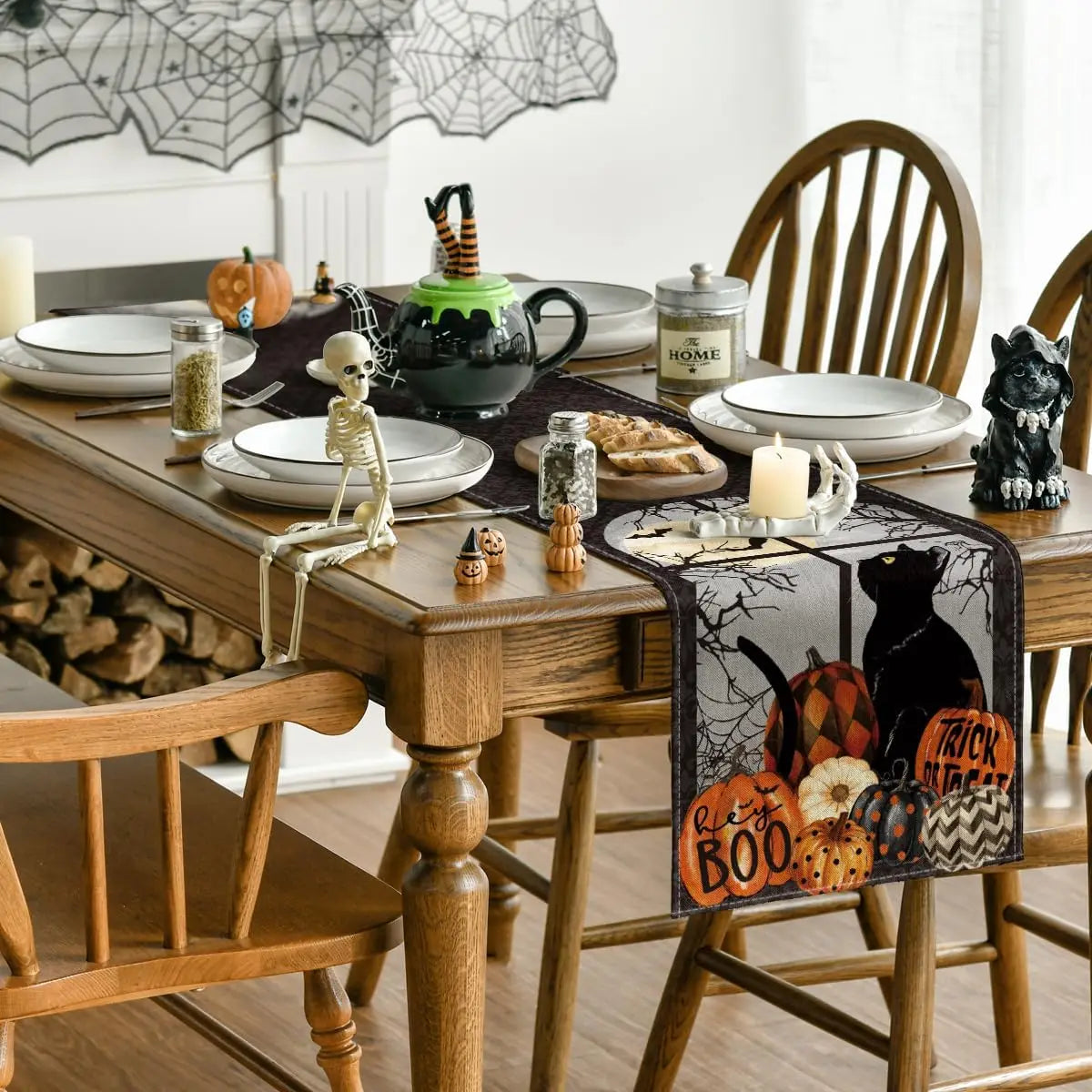 Cette image montre une table dressée pour l'Halloween, avec des décorations et accessoires thématiques tels que des citrouilles, des toiles d'araignée, un squelette et une théière verte.