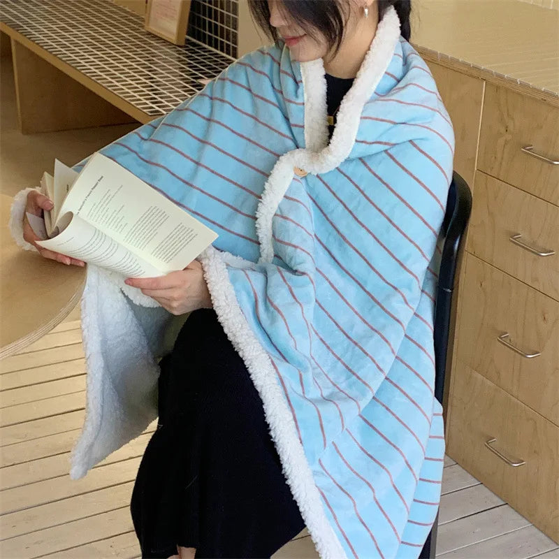 Une femme enveloppée dans une couverture rayée bleue et blanche semble lire un livre confortablement installée.