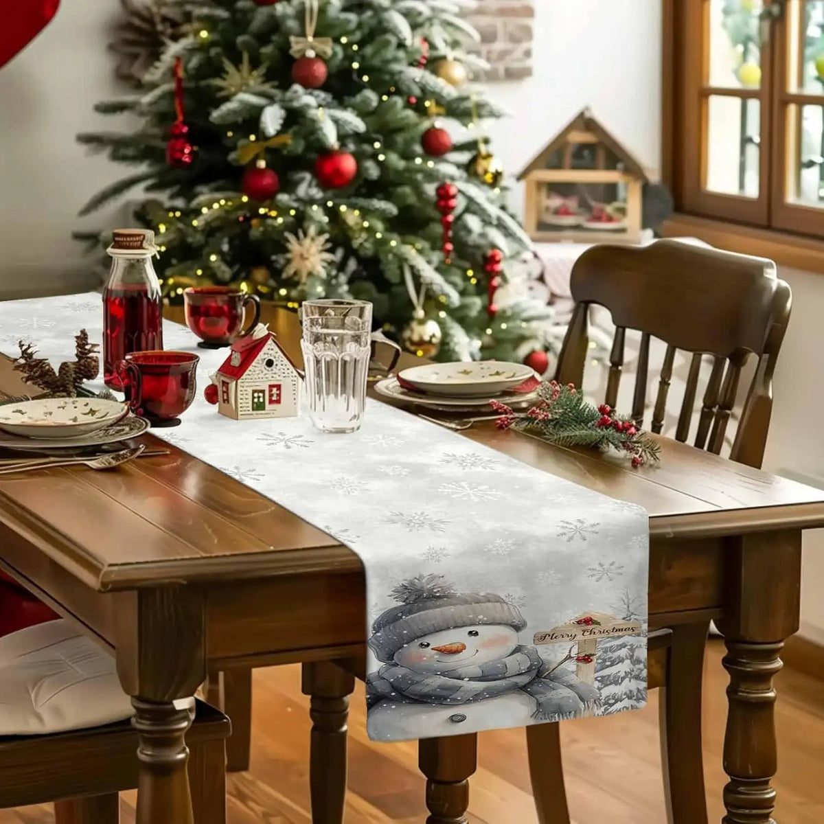 Une décoration de table de Noël accueillante avec un sapin illuminé, des décorations rouges et argentées, et une serviette de table avec un bonhomme de neige pour une ambiance festive.