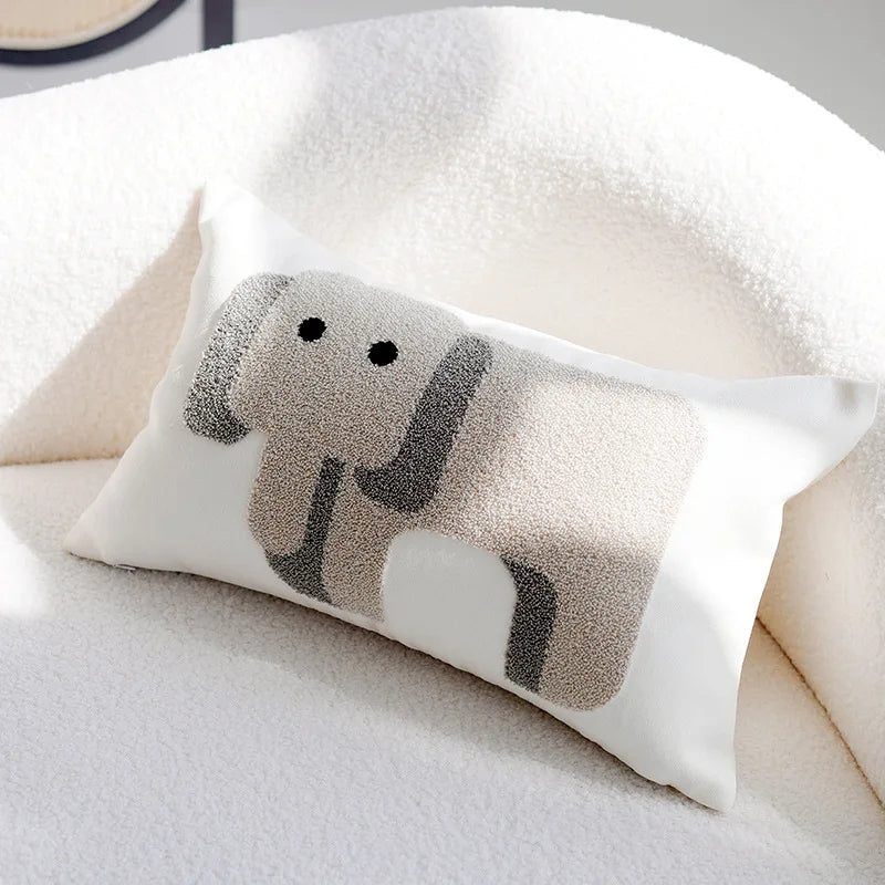 Un coussin décoratif de forme ovale avec un motif d'éléphant stylisé en noir et blanc, reposant sur un lit ou un canapé moelleux.