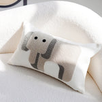 Un coussin décoratif de forme ovale avec un motif d'éléphant stylisé en noir et blanc, reposant sur un lit ou un canapé moelleux.