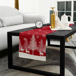 Élégant chemin de table rouge avec des motifs d'arbres et de rennes, posé sur une table basse noire dans un décor intérieur moderne et harmonieux.
