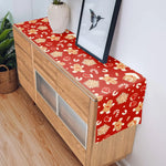 Meuble en bois avec un chemin de table décoré de motifs festifs rouges et dorés.